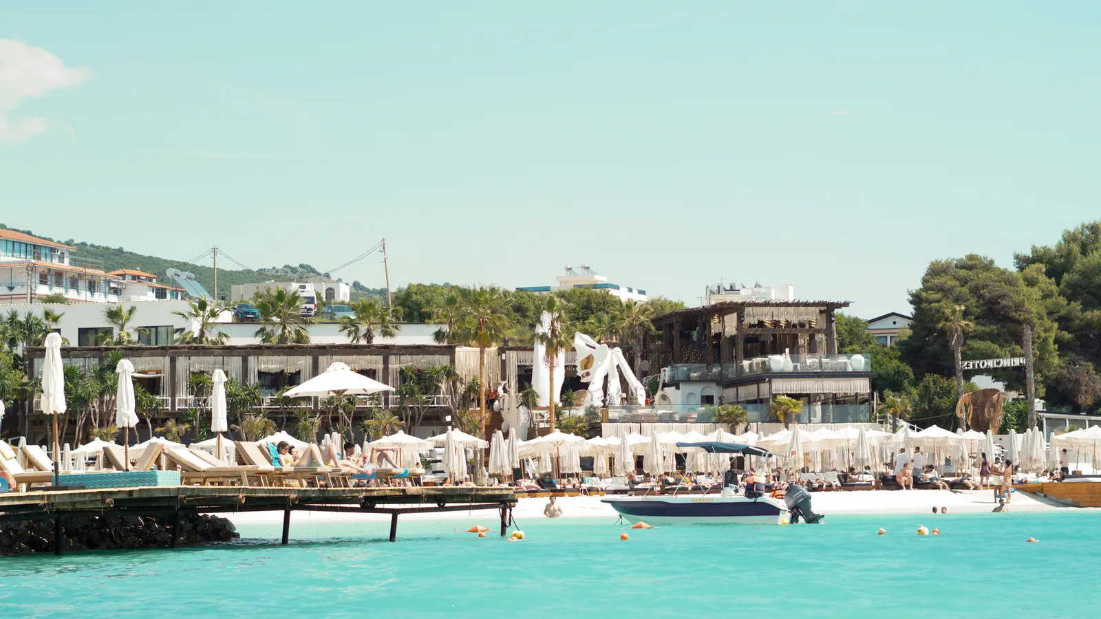 A lively beach club with straw umbrellas and boats above turquoise water at Ksamil, Albanian Riviera — book Albania tours and experiences